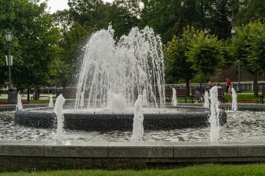 Polonya 'nın Krynica Zdroj kentindeki güzel manzaralı Spa Park manzarası. Modern doğrusal fıskiyeler ve parlak bir yaz gökyüzü altında kırmızı çatıları olan tarihi tatil köyleri. Seyahat ve rahatlama için ideal..