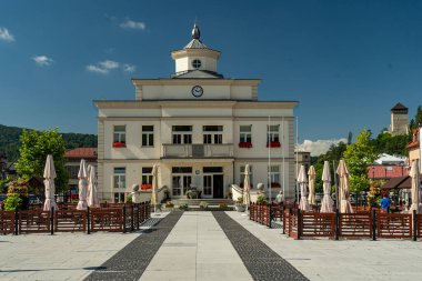 Muszyna, Küçük Polonya Voyvoda, Polonya - 05 Ağustos 2025 - Pazar Meydanı 'ndaki tarihi belediye binasının merkezi manzarası, açık bir yaz gökyüzü altında kafe bahçeleriyle çevrili.