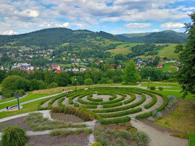 Muszyna, Malopolska Voyvodeship, Polonya - 08 Ağustos 2025 - Duyusal Bahçeler 'deki dairesel çit labirenti manzarası yükseldi ve arka planda orman tepeleri yer aldı..