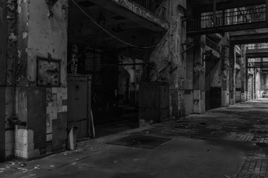 Zarar görmüş duvarları ve boş çalışma alanı olan harabe bir fabrikanın içindeki uzun karanlık koridor..