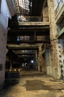 Terk edilmiş endüstriyel iç mekan, çok katlı korkuluklar ve hasarlı duvarlar..