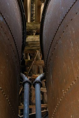 Terk edilmiş kazan dairesinin içinde büyük paslı metal tanklar ve dar servis yolları var..