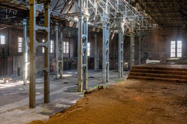 Metal parmaklıkları, duvarları ve bozulmuş mimari yüzeyleri olan terk edilmiş bir sanayi binasının iç manzarası.