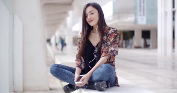 Жінка слухає музику в місті на лавці — стокове відео
