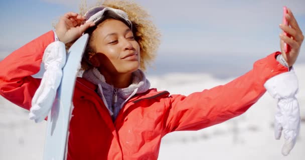 Woman carrying snowboard and taking selfie — Stok video