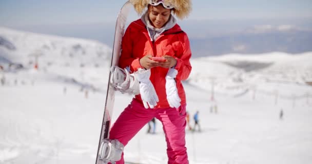 Женщина, несущая сноуборд и печатающая на мобильном — стоковое видео