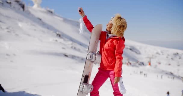 Woman carrying snowboard and taking selfie — 图库视频影像