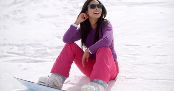 Женщина, сидящая в снегу с помощью сноуборда — стоковое видео