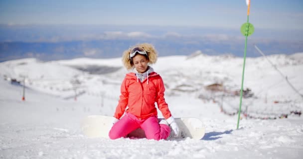 Женщина, сидящая в снегу с помощью сноуборда — стоковое видео