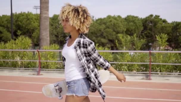 Женщина ходит со скейтбордом в руках — стоковое видео