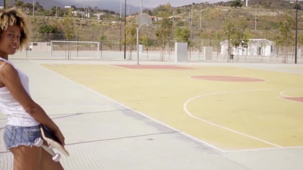 Frau steht mit Skateboard auf Basketballplatz — Stockvideo