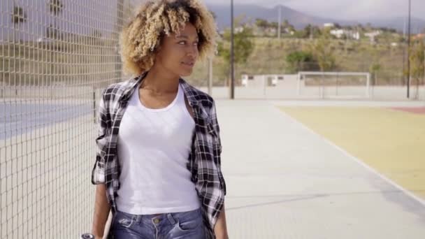 Женщина ходит со скейтбордом в руках — стоковое видео