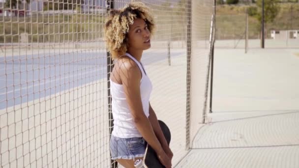 Жінка стоїть зі скейтбордом на баскетбольному майданчику — стокове відео