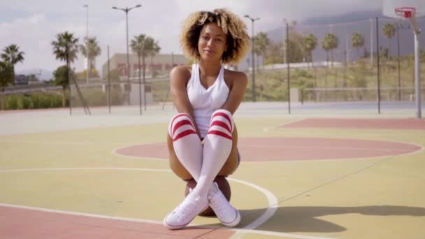 Femme assise sur un ballon de basket au court — Video