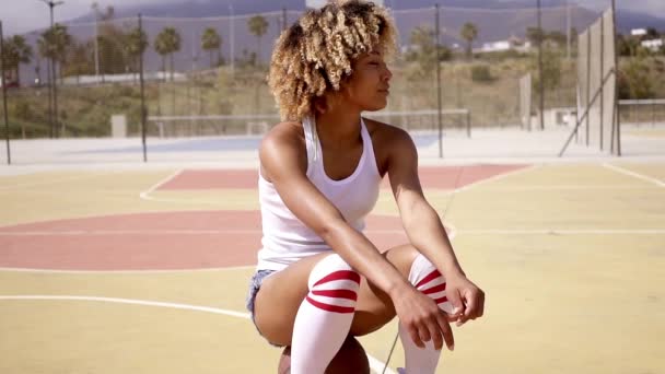 Mujer sentada en una pelota de baloncesto en la cancha — Vídeos de Stock