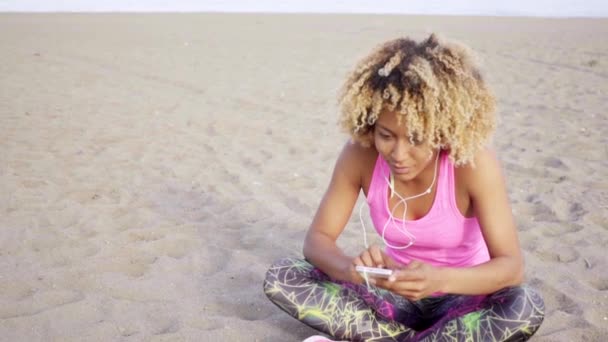 Женщина сидит на песке и слушает музыку — стоковое видео