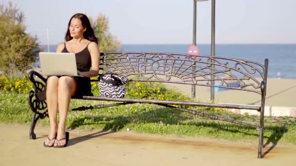 Vrouw die op laptop op aan het strand promenade werkt — Stockvideo