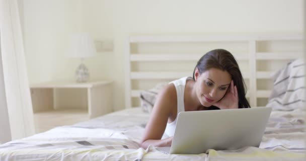 Mujer joven acostada en la cama con el ordenador portátil — Vídeos de Stock