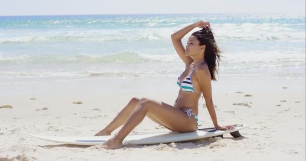 Женщина сидит на доске для серфинга на пляже — стоковое видео