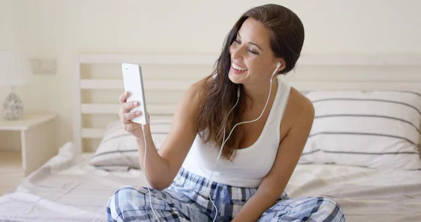 Mujer usando dispositivo con auriculares en la cama —  Fotos de Stock