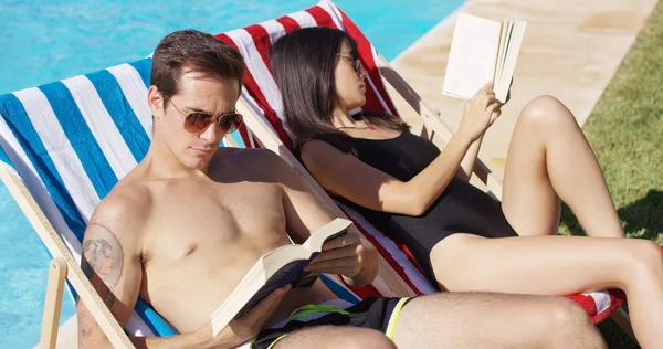 Atractiva pareja joven leyendo junto a la piscina —  Fotos de Stock