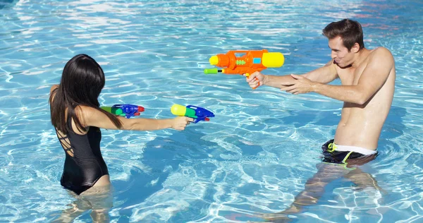 Pareja disparando armas de agua en la piscina —  Fotos de Stock