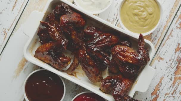Csirkeszárnyak sűrű barbecue szósszal, különböző oldalsó mártásokkal. Fehér öntöttvas tálcán tálalva — Stock videók