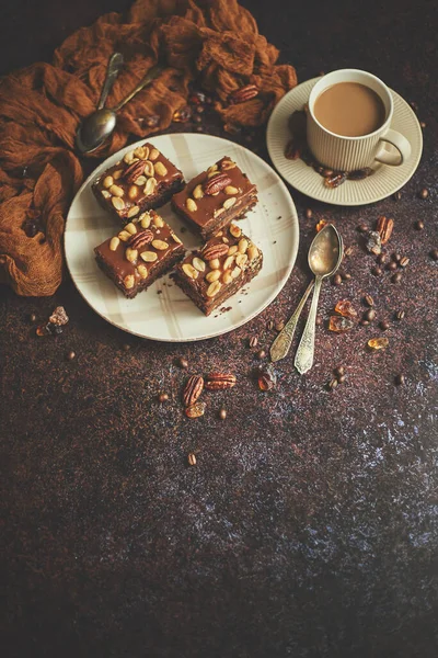 Квадратные кусочки вкусного карамельного торта с арахисом и бразильскими орехами подаются с молочным кофе — стоковое фото