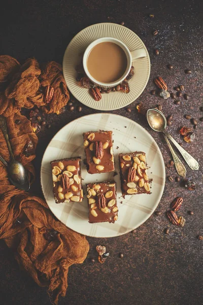 Chokladkaka med karamell glasyr, pekannötter och varmt kaffe, på rustik bakgrund. Nybakat — Stockfoto
