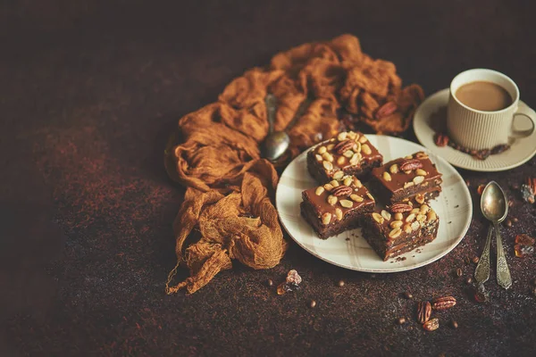 Los trozos cuadrados de delicioso pastel de caramelo con cacahuetes y nueces brasileñas servidas con café con leche —  Fotos de Stock