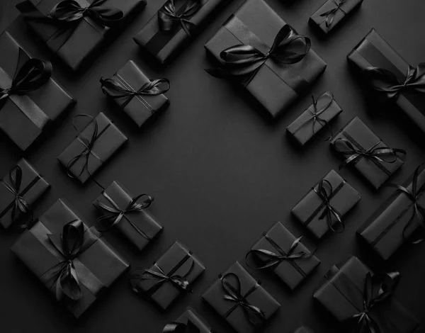 Cadeaux arrangés boîtes enveloppées dans du papier noir avec ruban noir sur fond noir. Concept de Noël — Photo