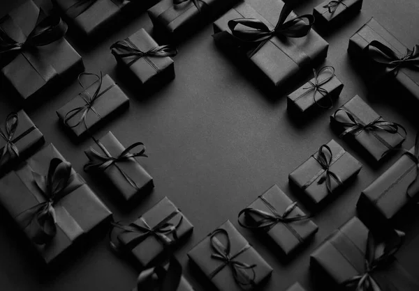 Cadeaux arrangés boîtes enveloppées dans du papier noir avec ruban noir sur fond noir. Concept de Noël — Photo