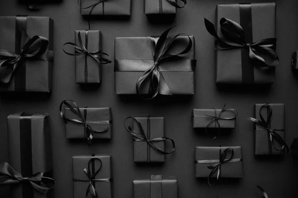 Thème de Noël sombre. Cadeaux carrés en boîte enveloppés dans du papier noir et un ruban disposés sur du noir — Photo