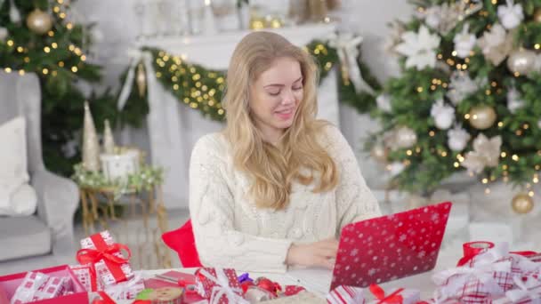Молодая блондинка делает покупки в Интернете с помощью ноутбука на фоне Рождества — стоковое видео