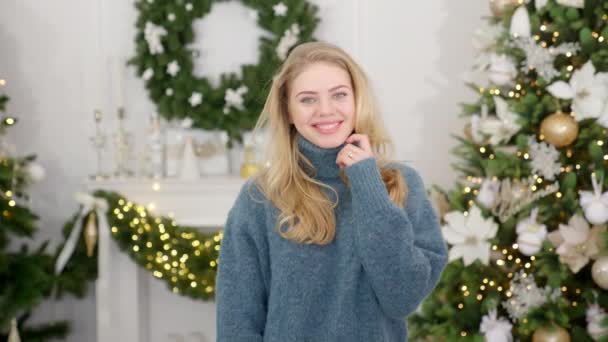 Μοντέρνα χαμογελαστή γυναίκα που φοράει πλεκτό πουλόβερ μπροστά από το χριστουγεννιάτικο δέντρο — Αρχείο Βίντεο