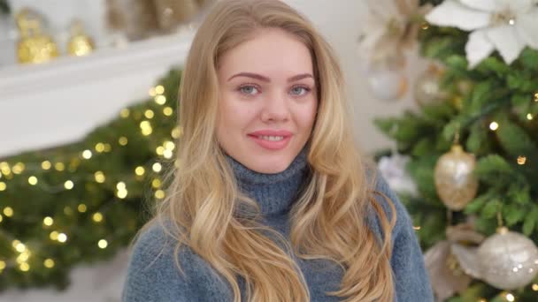 Модная улыбающаяся женщина в вязаном уютном свитере перед рождественской елкой — стоковое видео