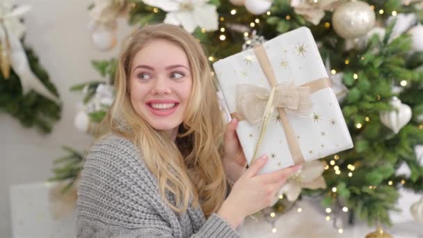 Surprised and happy young woman with christmas present box near christmas tree. — Stock Video