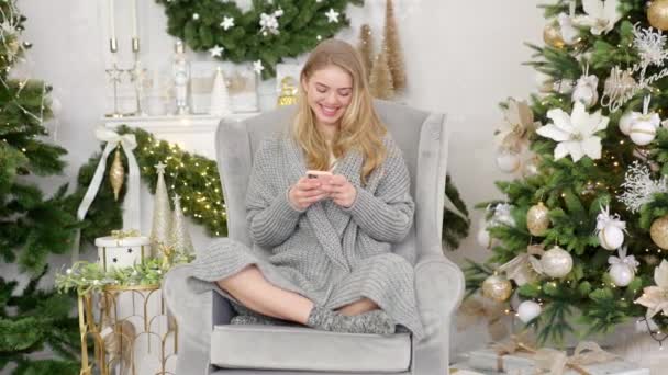 Senyum trendi wanita di abu-abu nyaman sweater duduk di kursi yang nyaman dan mengirim pesan teks — Stok Video