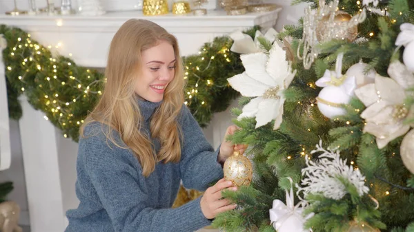 Glückliche junge blonde Frau schmückt Weihnachtsbaum zu Hause mit Ball — Stockfoto