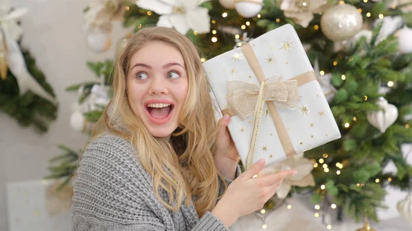Zaskoczona i szczęśliwa młoda kobieta z pudełkiem prezentów świątecznych w pobliżu choinki. — Zdjęcie stockowe