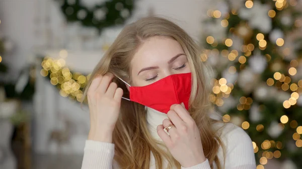 Fáradt nő vegye le védő maszk, miközben áll ünnepi díszített otthon karácsonyra — Stock Fotó
