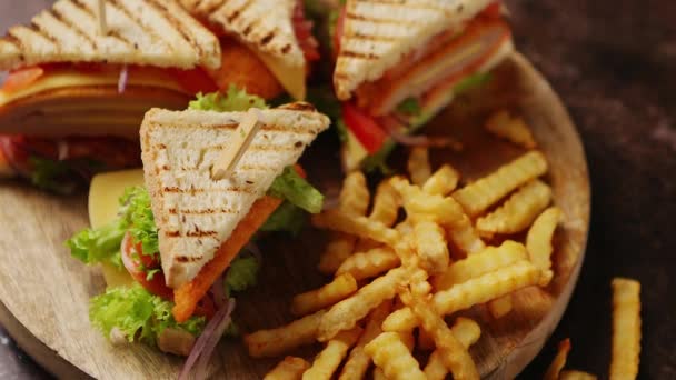 Sanduíches de clube servidos em uma tábua de madeira. Com batatas fritas quentes — Vídeo de Stock