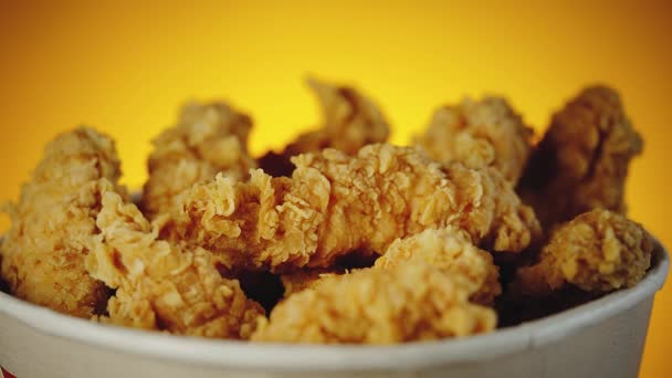 Bucket of crispy golden chicken wings, legs and strips. Side view over orange background — Stock Video