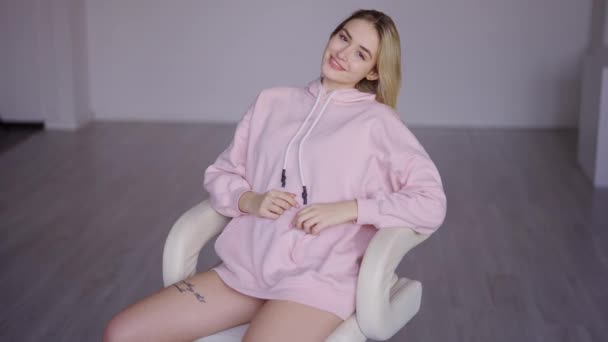 Young woman in hoodie sitting in armchair — Stock Video