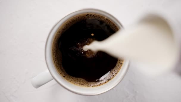 Het toevoegen van room aan een kopje met zwarte, hete koffie geplaatst op witte tafel — Stockvideo