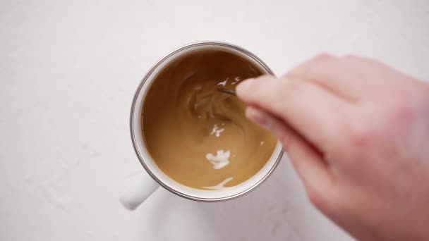 Mans ruka míchání kávy s mlékem v bílém kovovém šálku na bílém stole — Stock video