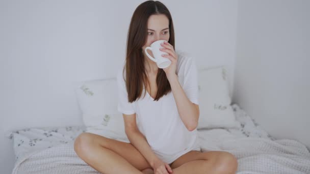 Femme calme inspirée boire une boisson chaude sur le lit le matin — Video