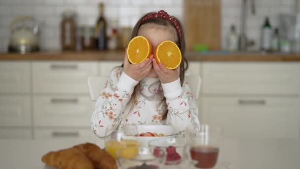 Liten flicka med färsk apelsin har roligt under frukost — Stockvideo
