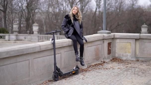 Mujer descansando cerca de scooter eléctrico en el parque — Vídeo de stock