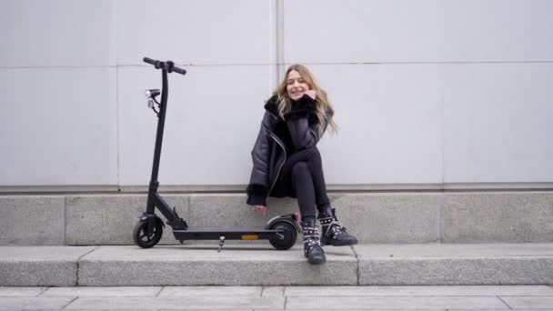 Happy female with scooter resting on sidewalk — ストック動画